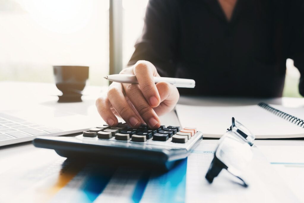 A woman is using a calculator at a desk to conduct an energy audit, unveiling the power of efficiency in Australian businesses.