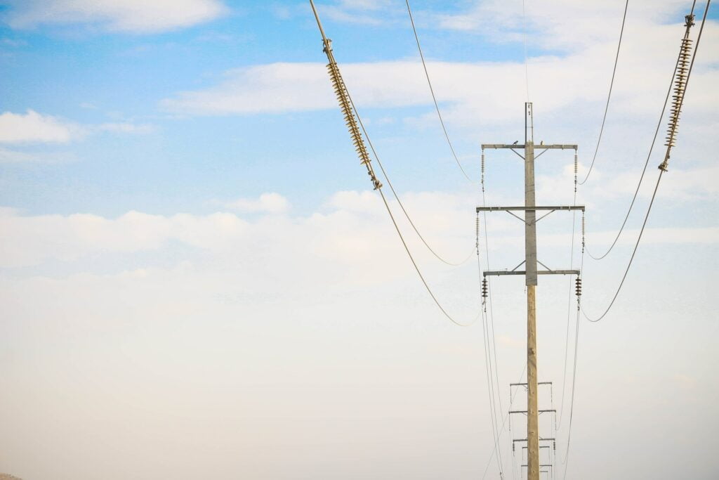 A power pole with wires suspended against a blue sky, highlighting the truth behind electric current.