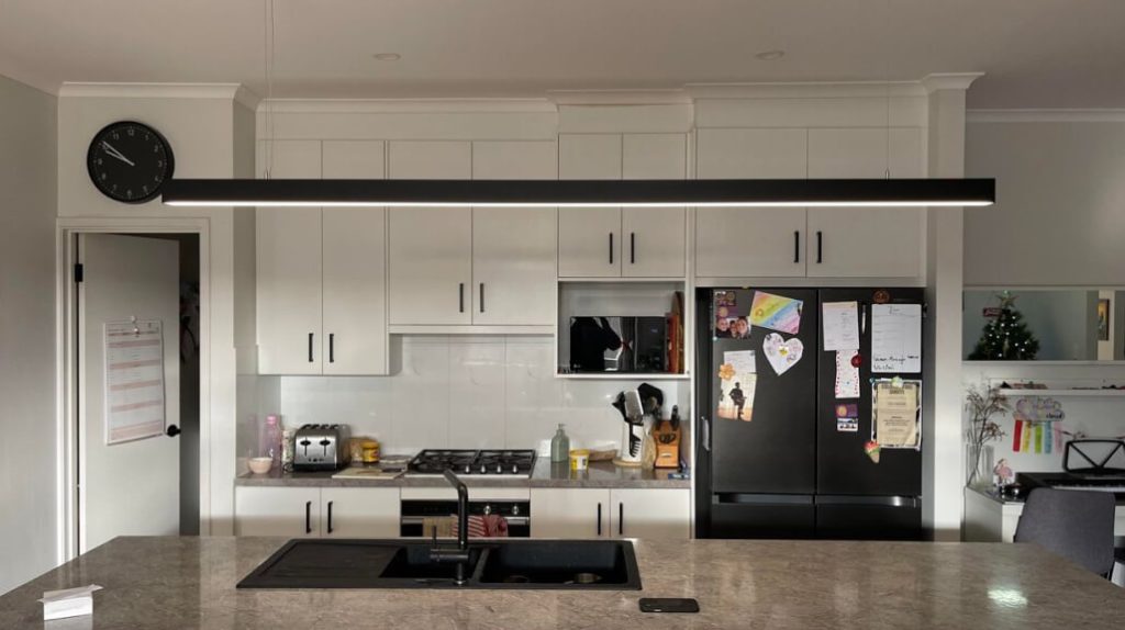 Modern kitchen with white cabinets, black appliances, a wall clock, and a marble countertop with a sink; family notes and art on the fridge.
