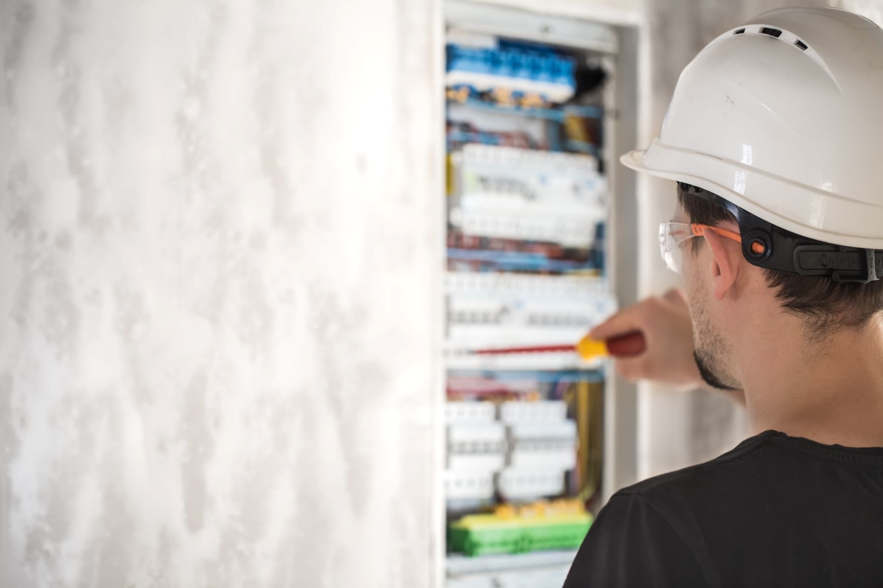 A man in a hard hat is working on an electrical panel.